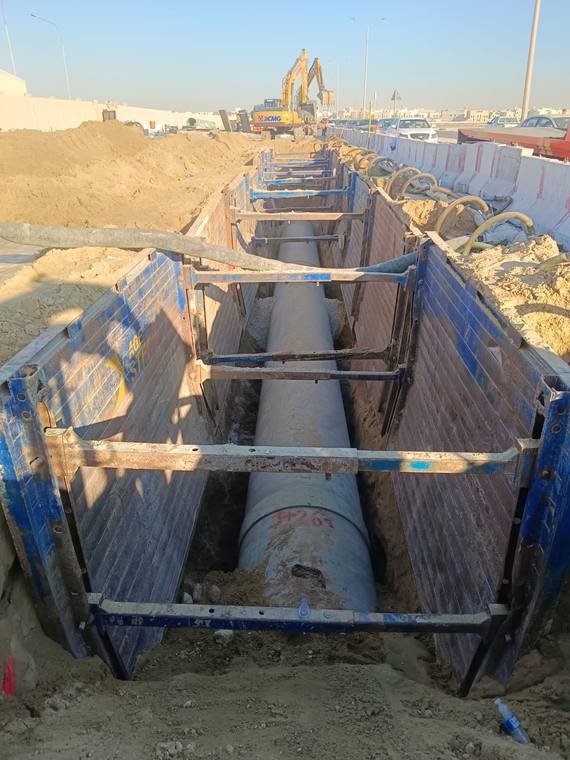 شركة وادي البناء الحديث – تنزيل أنبوب خرساني مسلّح RCP كبير القطر داخل خندق مدعّم بصناديق التدعيم.